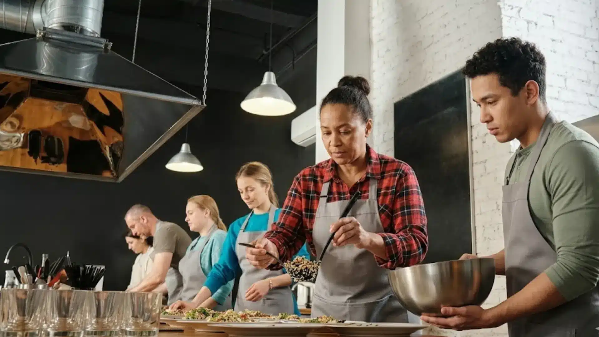 Cooking challenge with group preparing food together in modern kitchen wearing aprons and following instructor