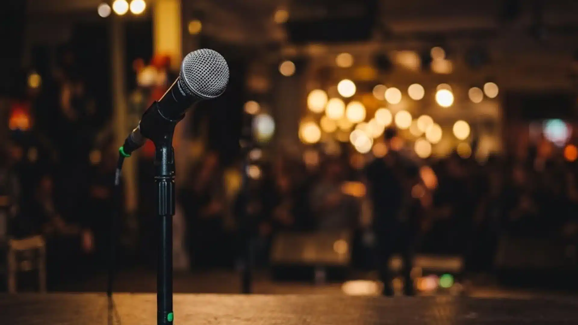 Microphone on stage with blurred audience and warm lights in background at live event or performance venue
