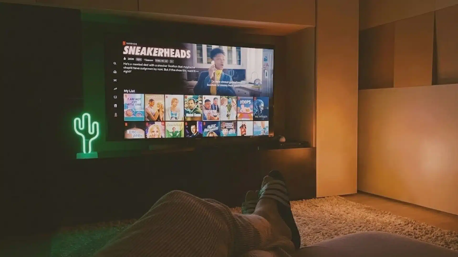 Person relaxing on couch watching streaming content on TV with cozy lighting and modern living room setup