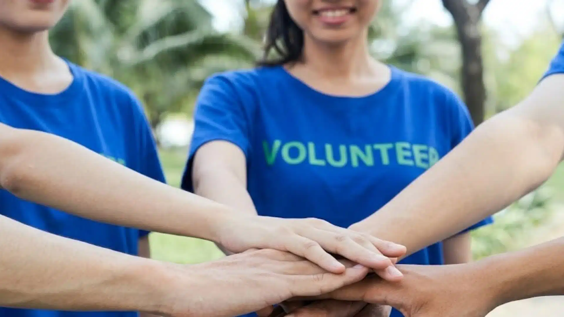 Volunteers stacking hands together outdoors wearing blue shirts showing teamwork and community support