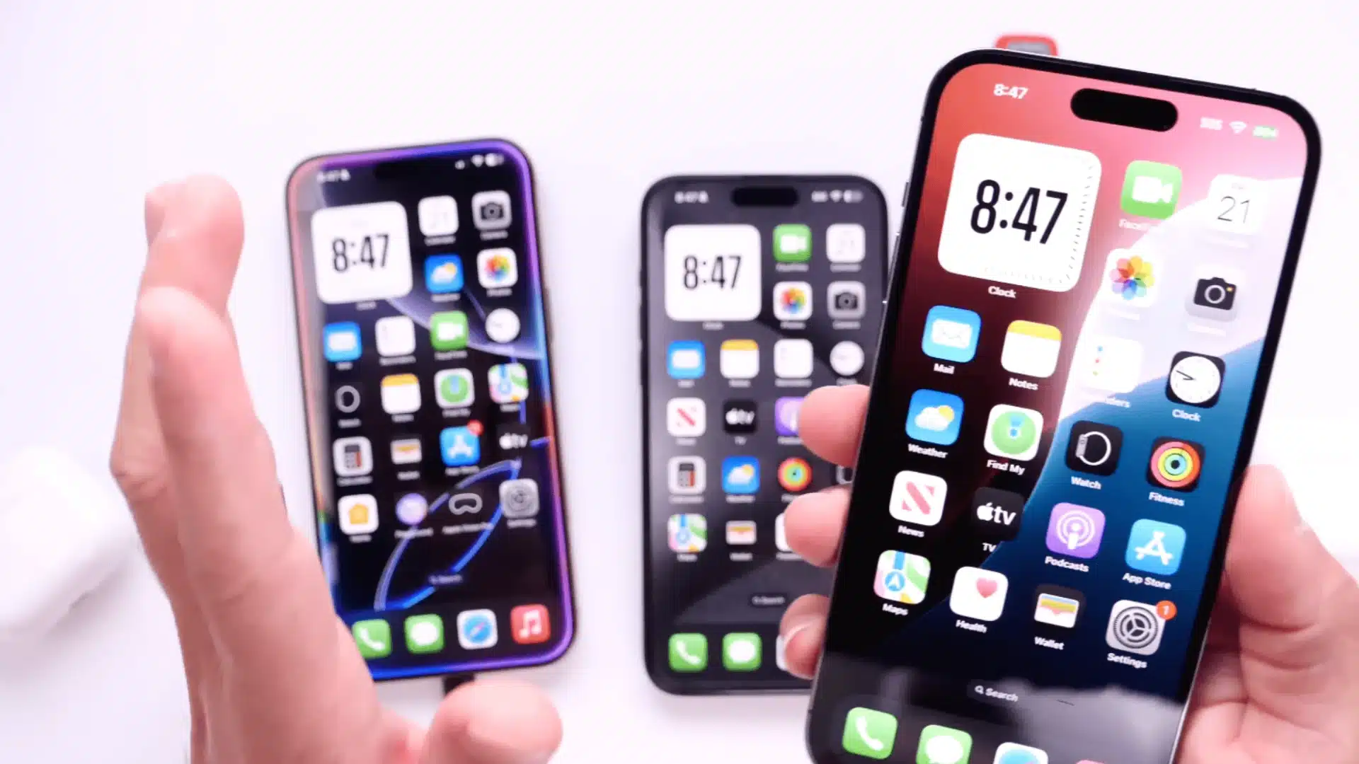 Hand holding iPhone with home screen visible while comparing multiple iPhone models side by side