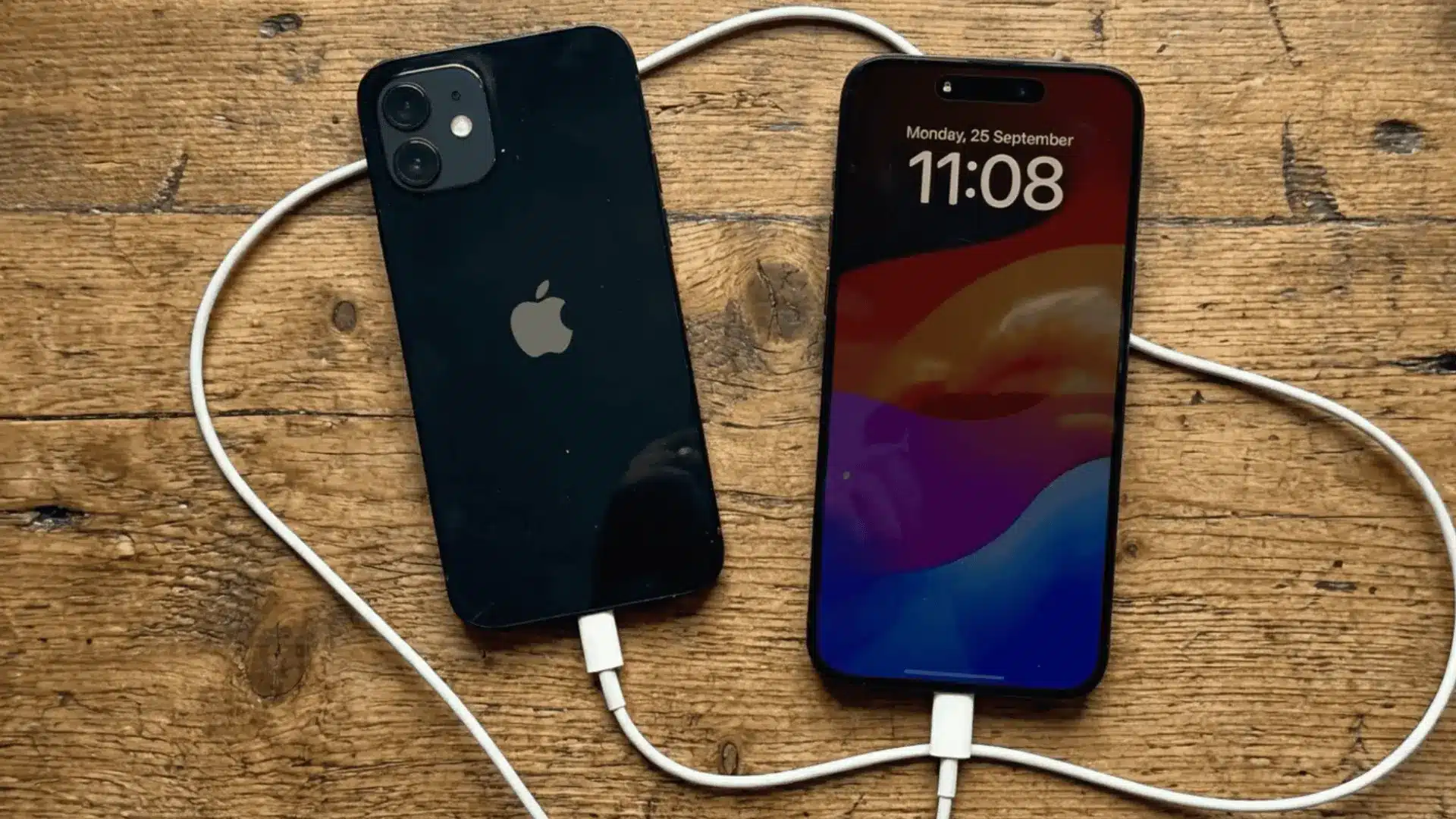 Two iPhones connected with charging cable on wooden surface showing device to device charging setup
