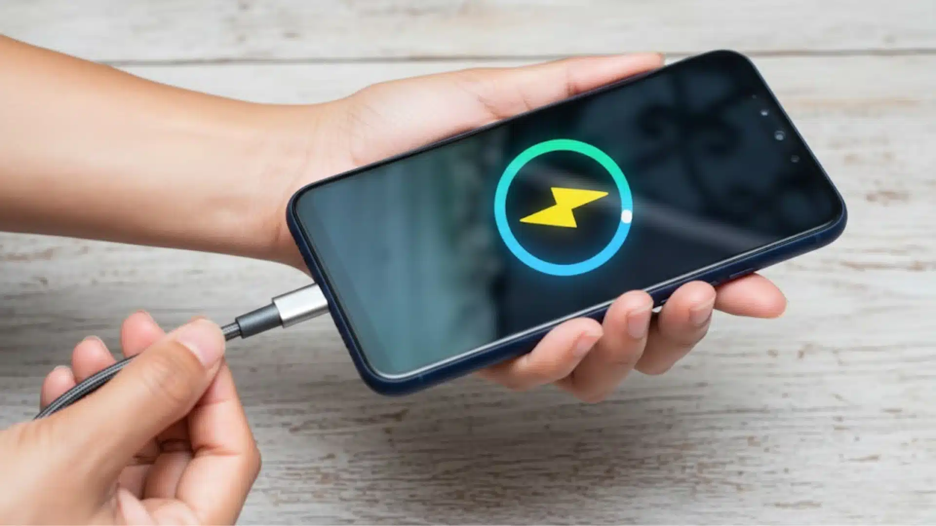 Hand holding smartphone while plugging charger showing battery charging icon on screen indicating power boost