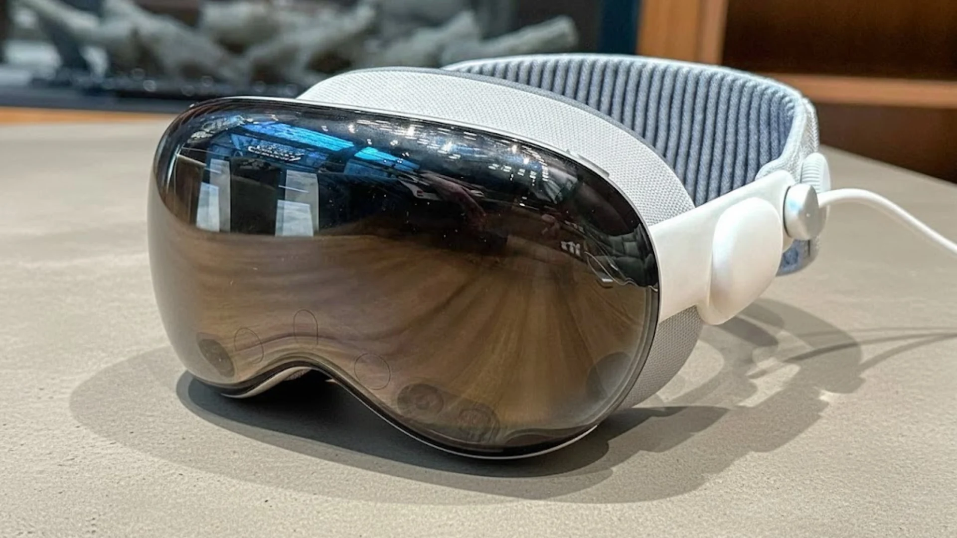 Apple Vision Pro headset resting on a table, showing curved glass front, white strap, and sleek mixed reality design