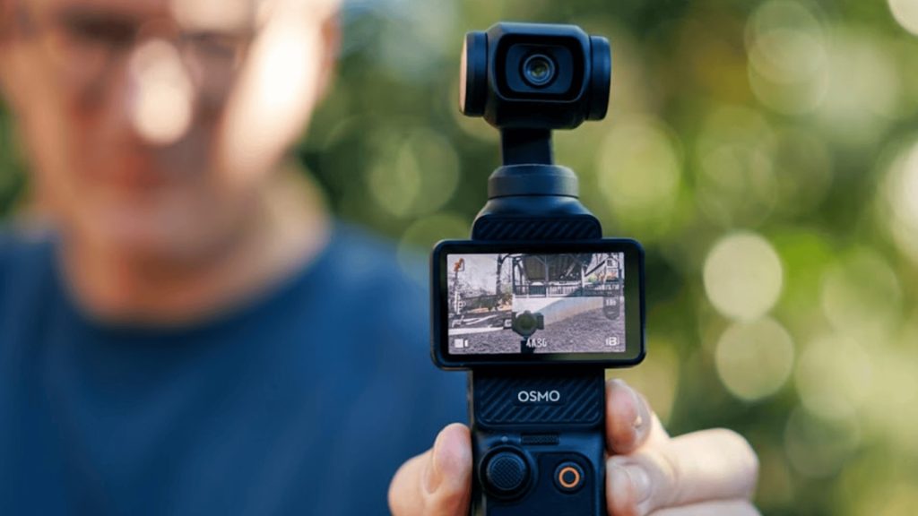 DJI Osmo Pocket 3 handheld gimbal camera recording outdoors with screen visible and blurred background