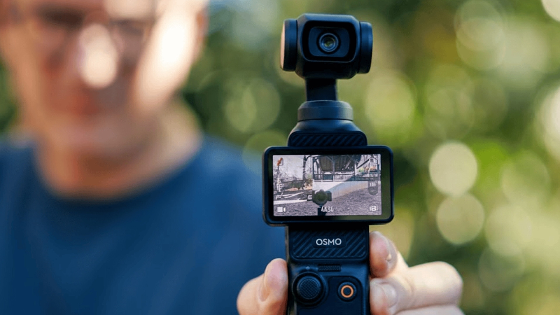 DJI Osmo Pocket 3 handheld gimbal camera recording outdoors with screen visible and blurred background