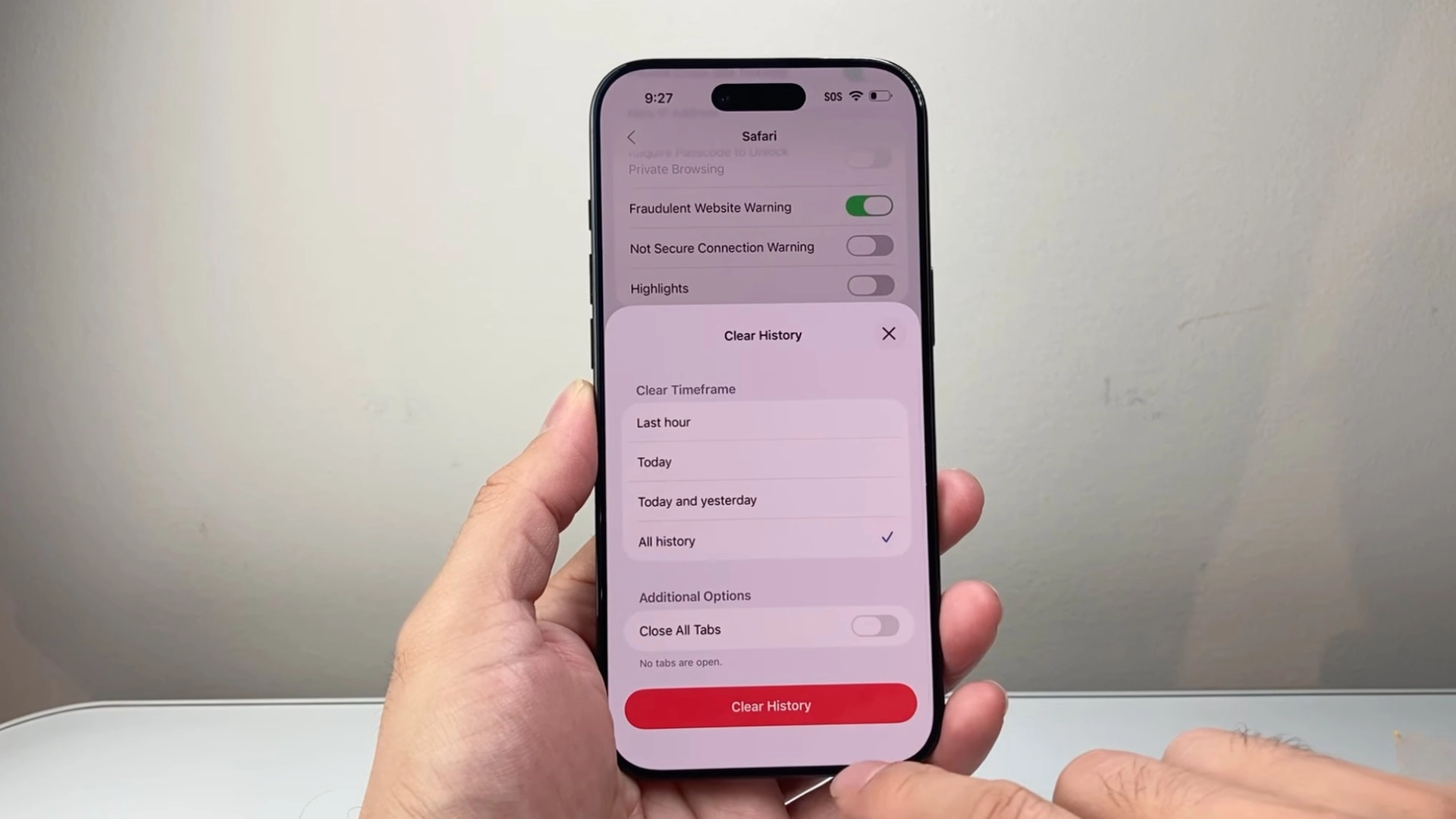 Hand holding iPhone showing Safari clear history screen with options to delete browsing data and close all tabs