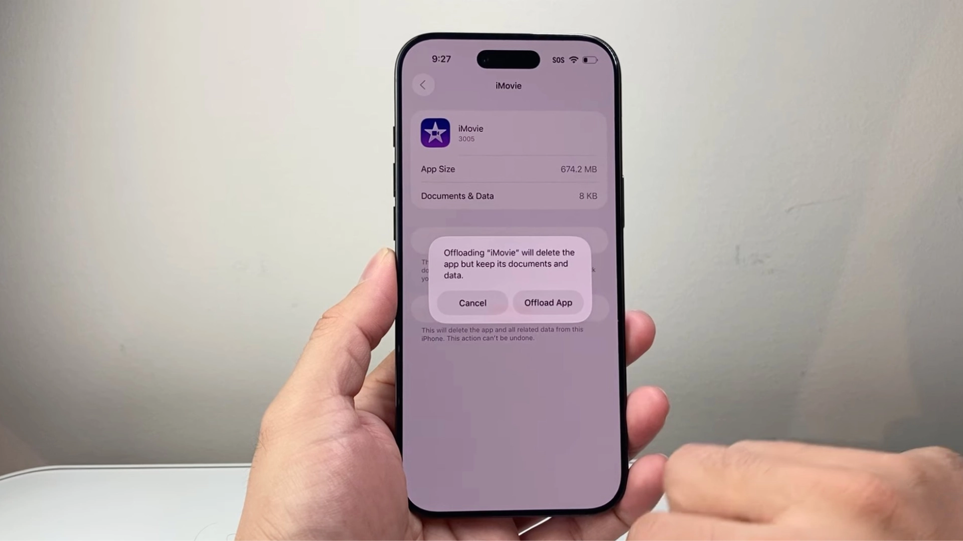 Hand holding iPhone showing iMovie storage screen with offload app option to clear cache without deleting documents and data