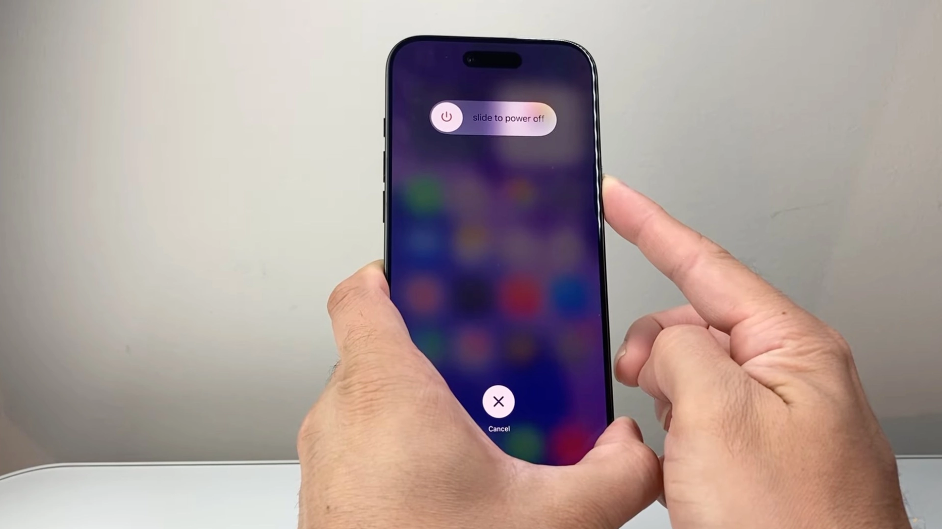 Hand holding iPhone showing slide to power off screen with power slider and cancel button visible