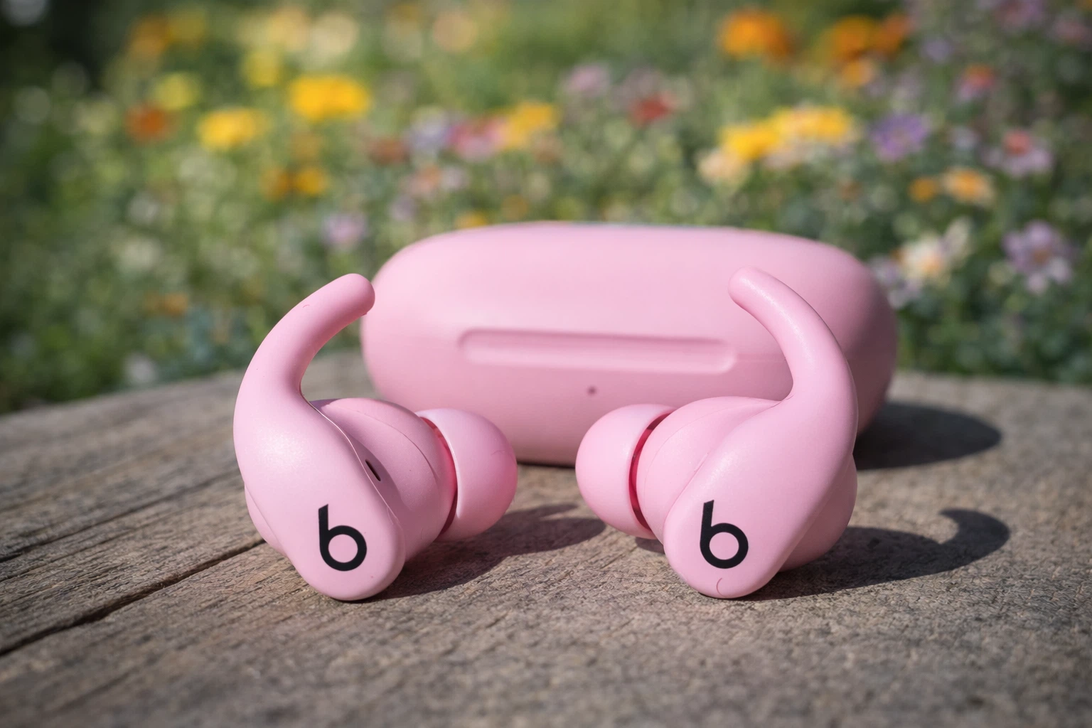 Beats Powerbeats Fit pink wireless earbuds with charging case on outdoor wooden surface