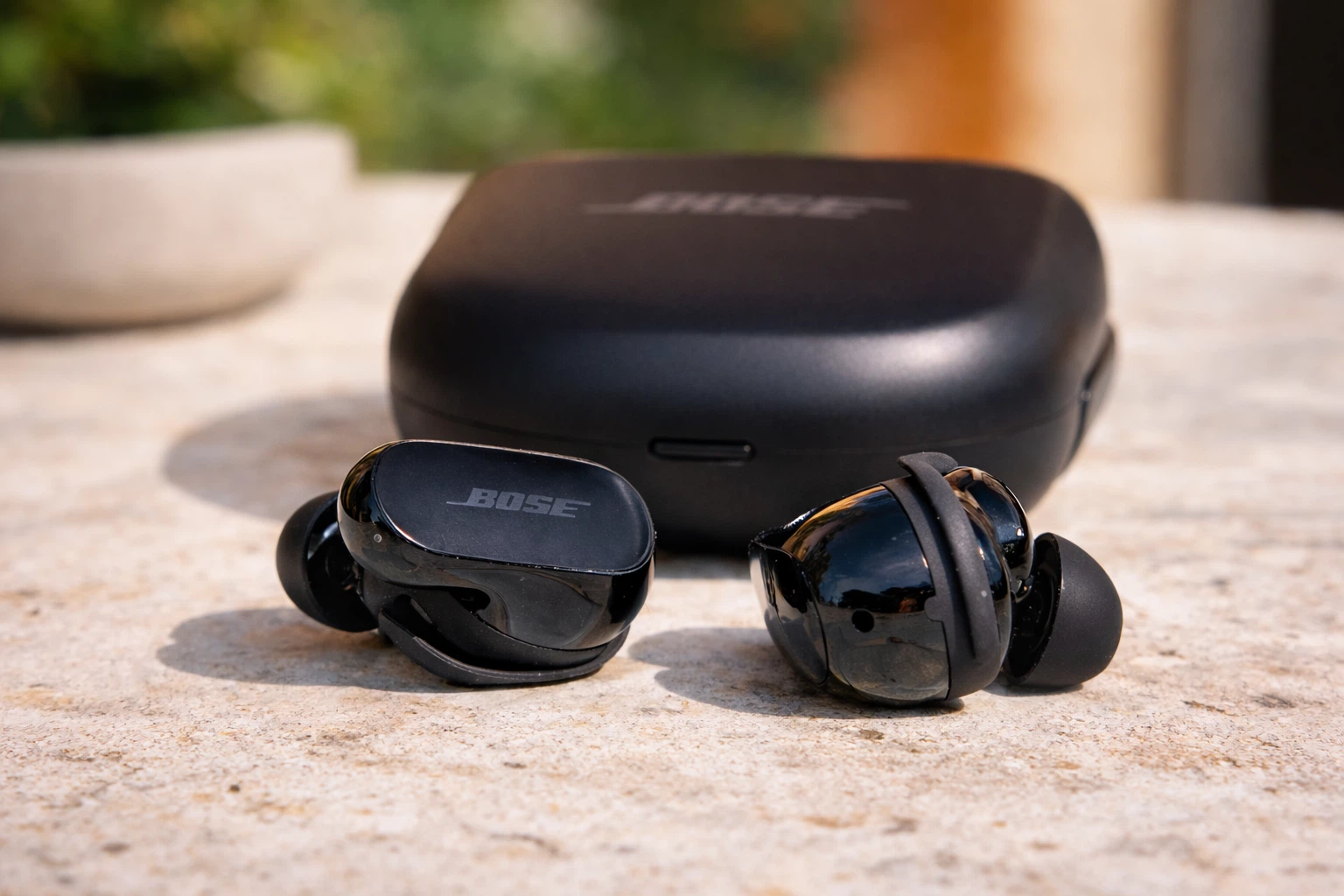 Black Bose QuietComfort Ultra Earbuds outside charging case on stone surface