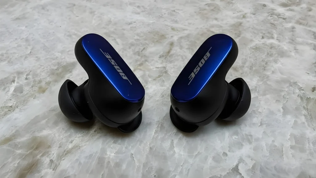 Bose QuietComfort Ultra earbuds in blue and black placed on marble surface close up