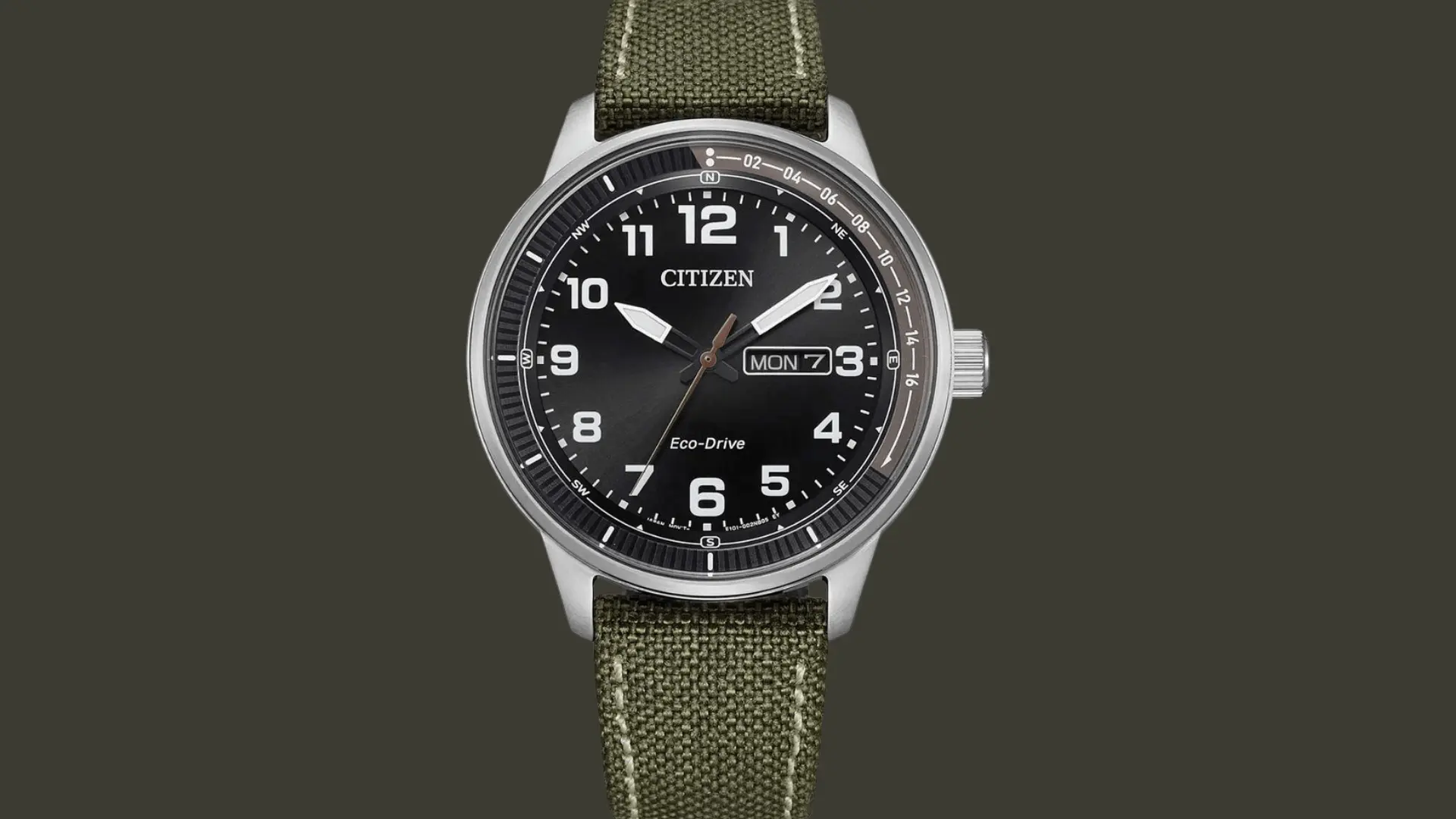 Citizen Eco Drive field watch with black dial, day date display, and green fabric strap on a dark background