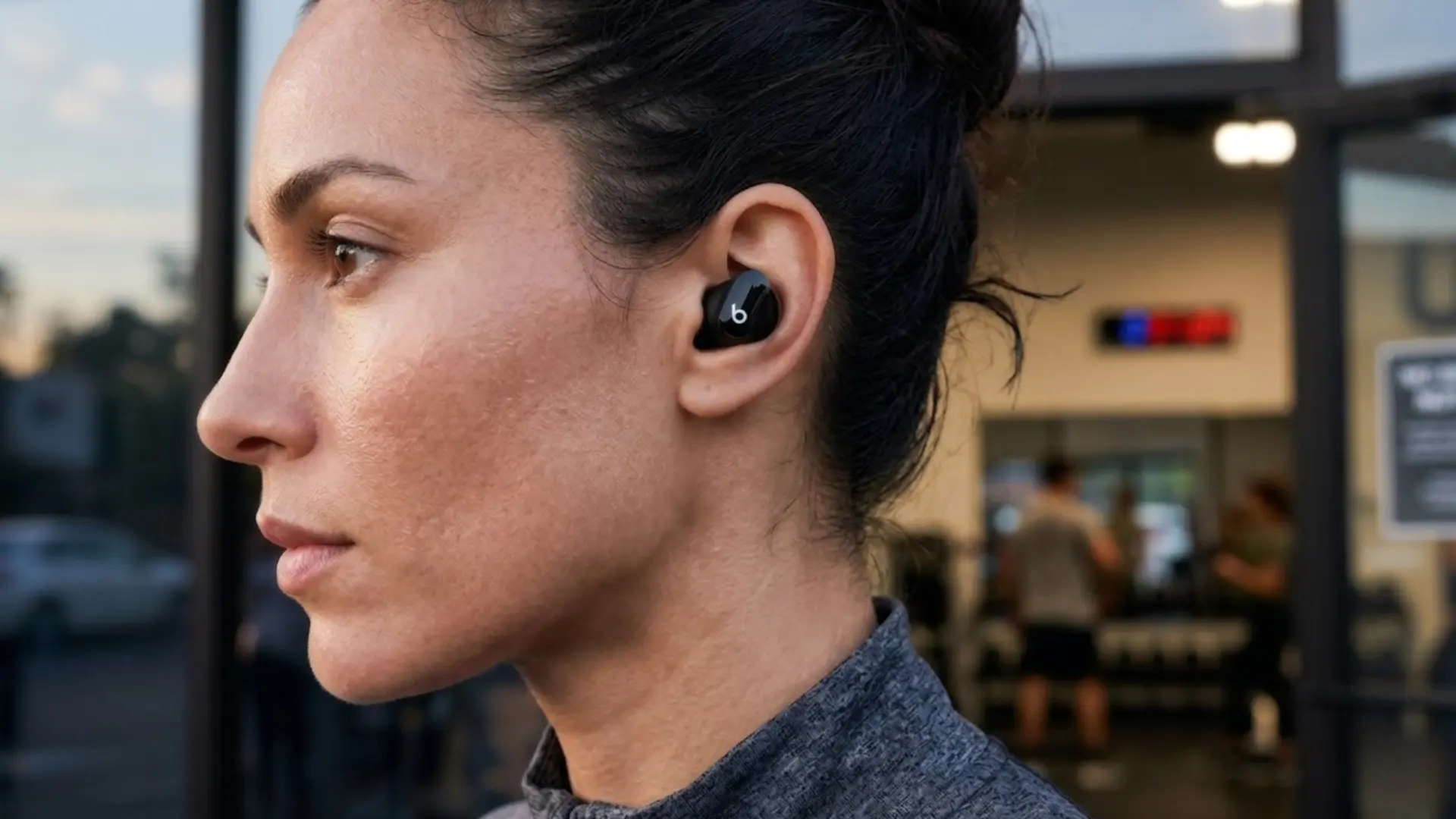 Close-up photograph of a woman wearing Beats Studio Buds Plus in gym attire showing design and comfort of the earbuds for daily use
