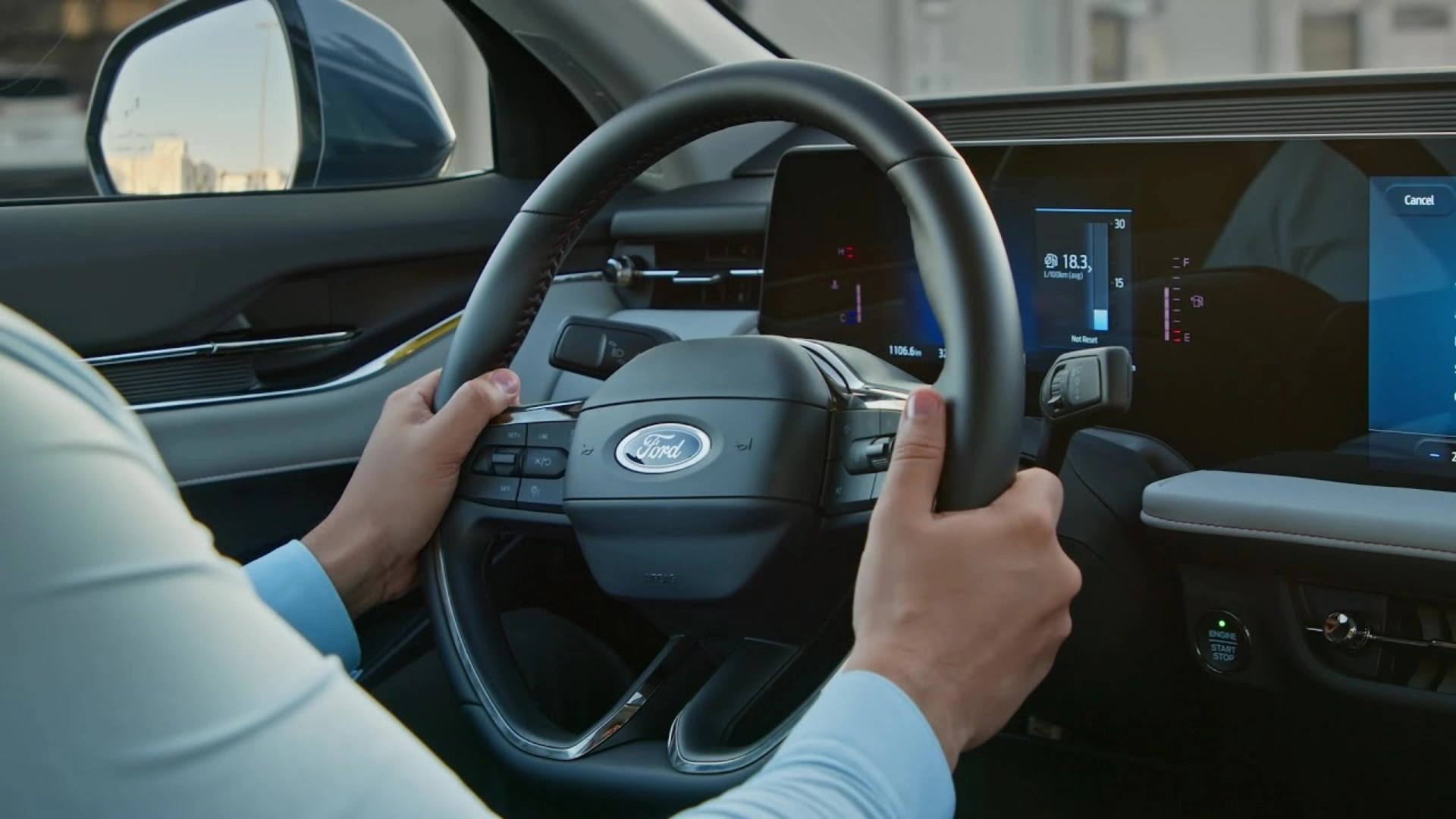 Driver holding Ford steering wheel with digital dashboard display inside a modern vehicle cabin