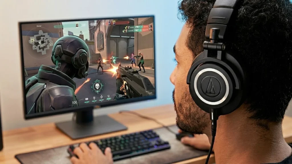Gamer wearing over ear good gaming headset while playing shooter game on desktop monitor with keyboard and mouse