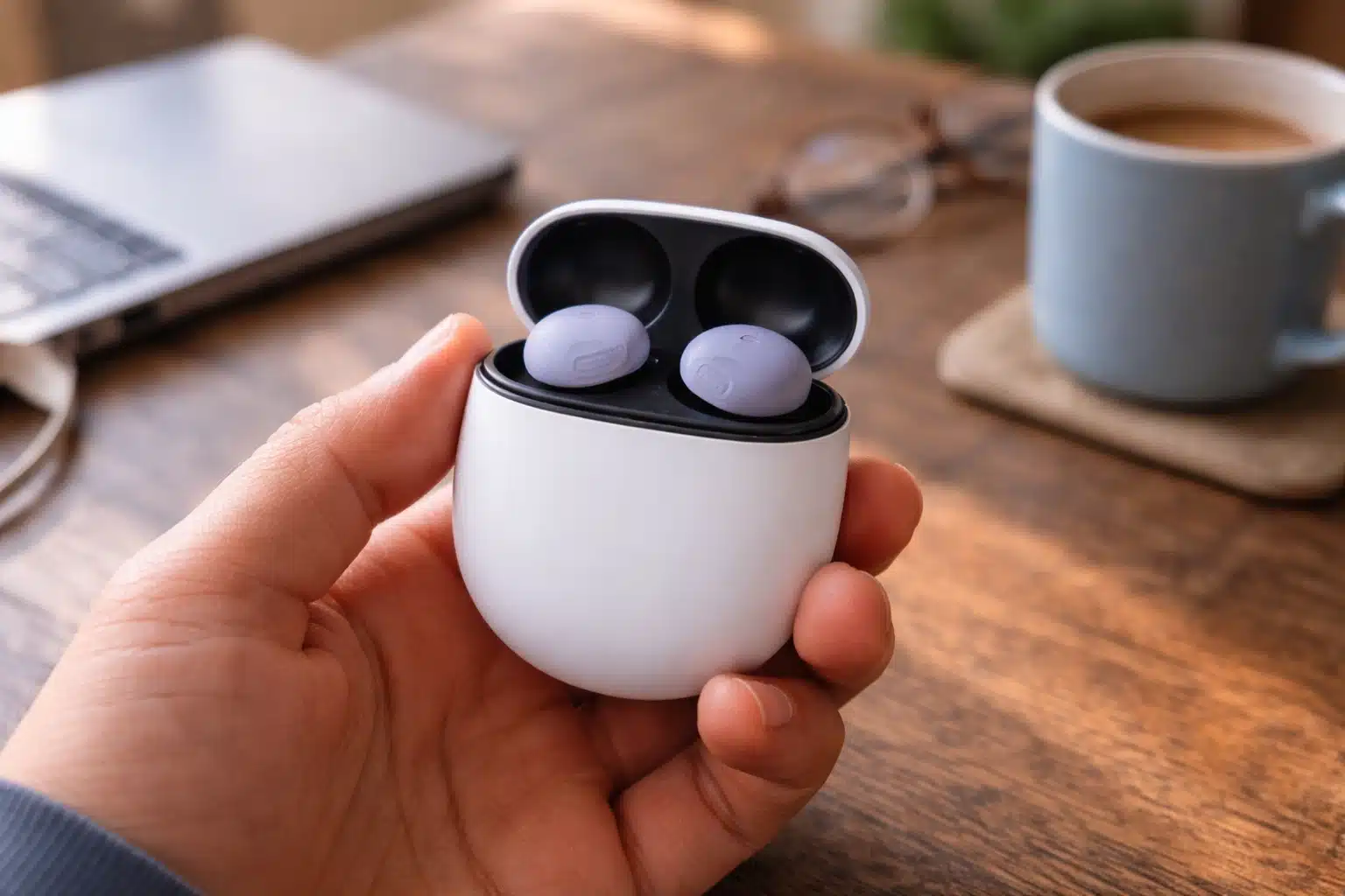 Google Pixel Buds Pro 2 in open charging case held in hand on wooden desk