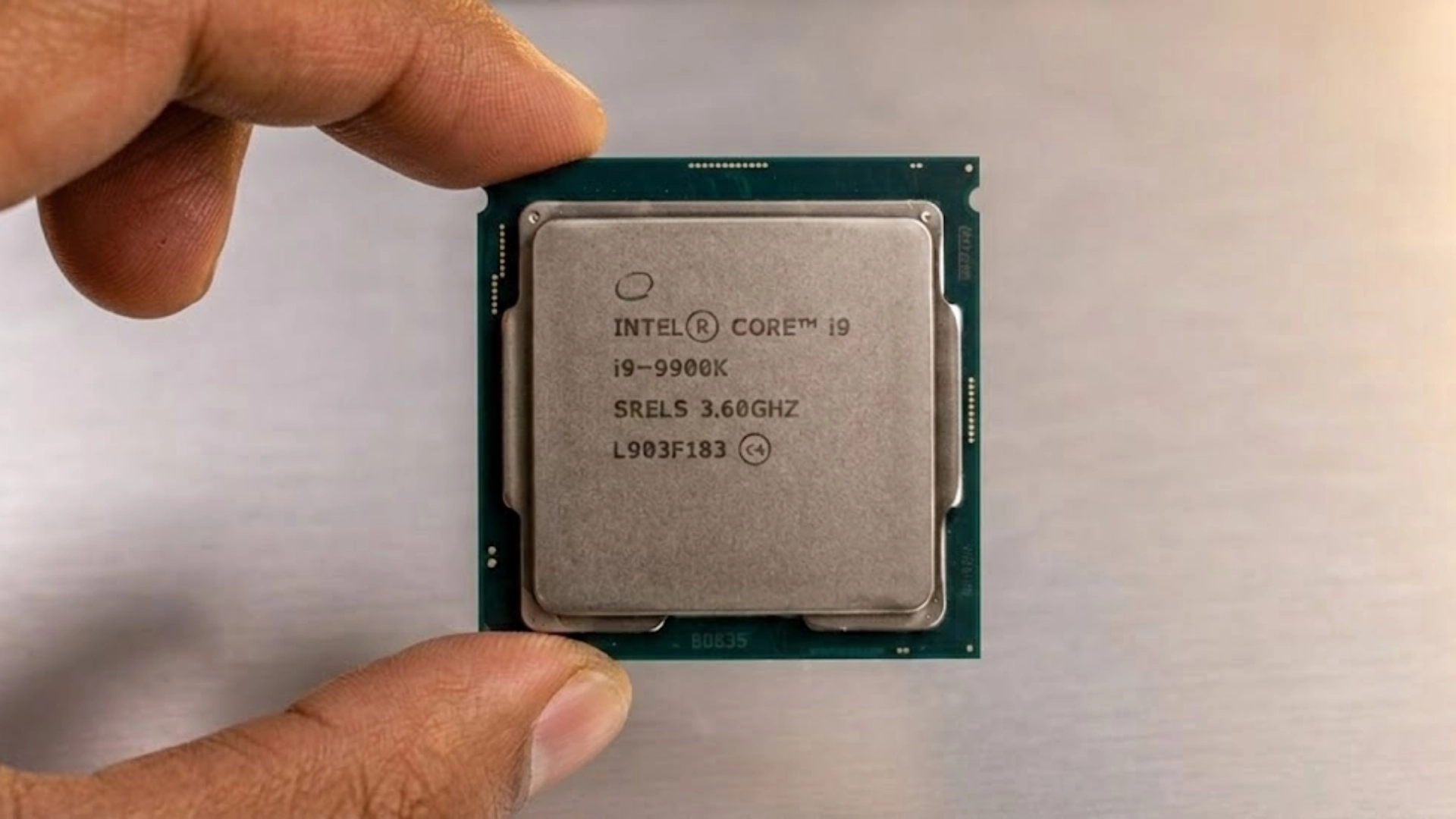 Hand holding Intel Core i9 9900K processor chip against wooden background close up view