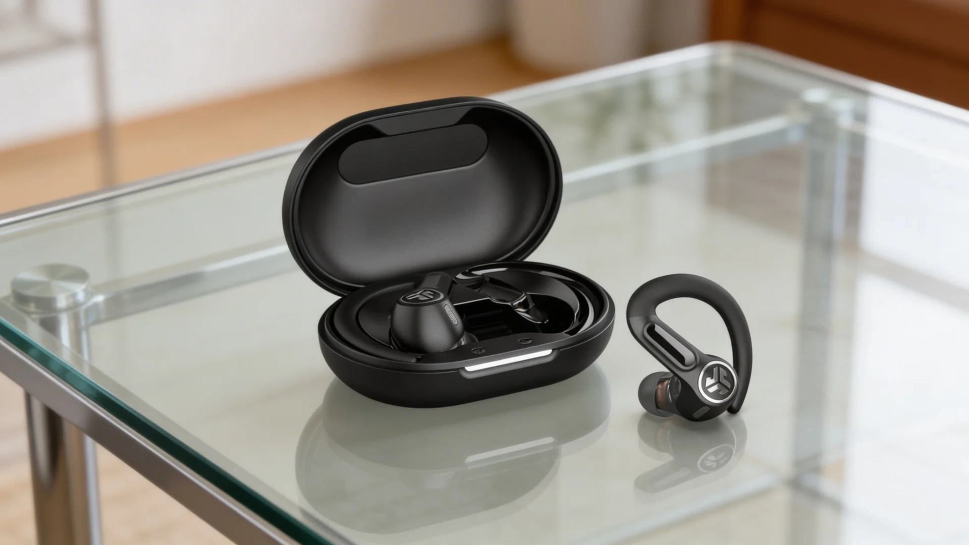 JLab Epic Air Sport ANC earbuds with ear hook next to open charging case placed on glass table for workout use