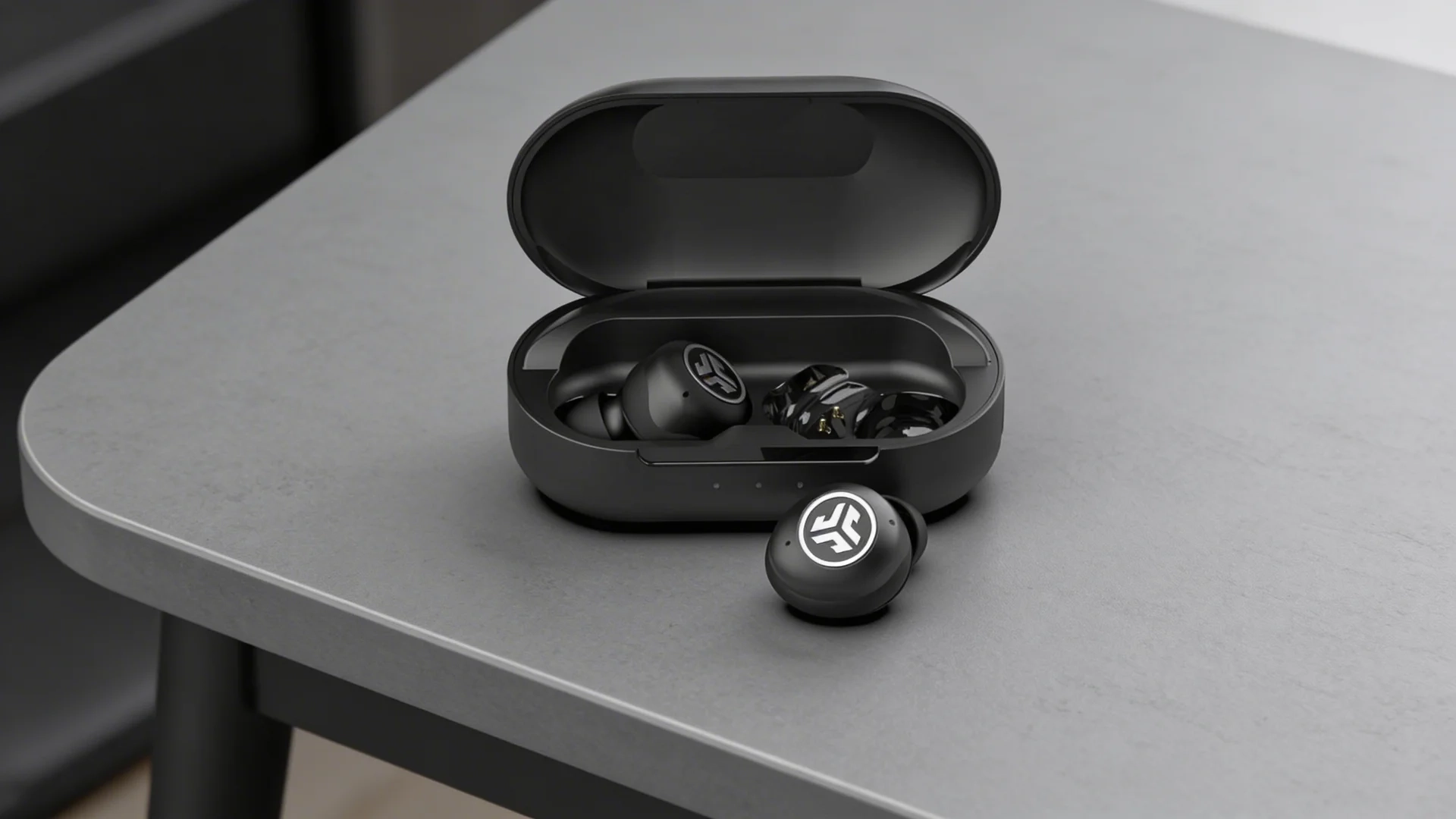 JLab JBuds Air Pro wireless earbuds in open charging case placed on a table with one earbud positioned outside the case