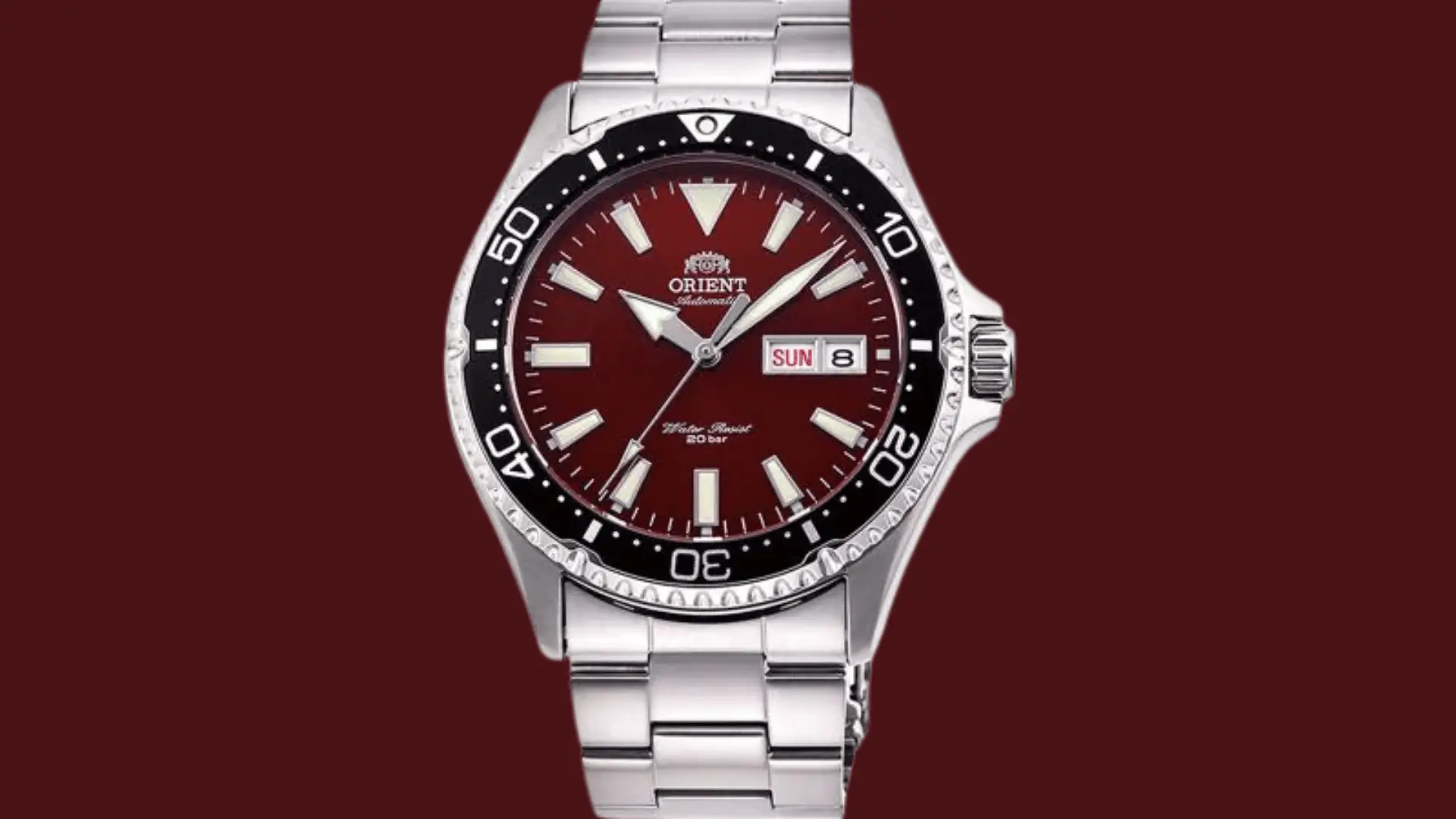 Orient automatic diver watch with red dial, day date window, and stainless steel bracelet on a red background