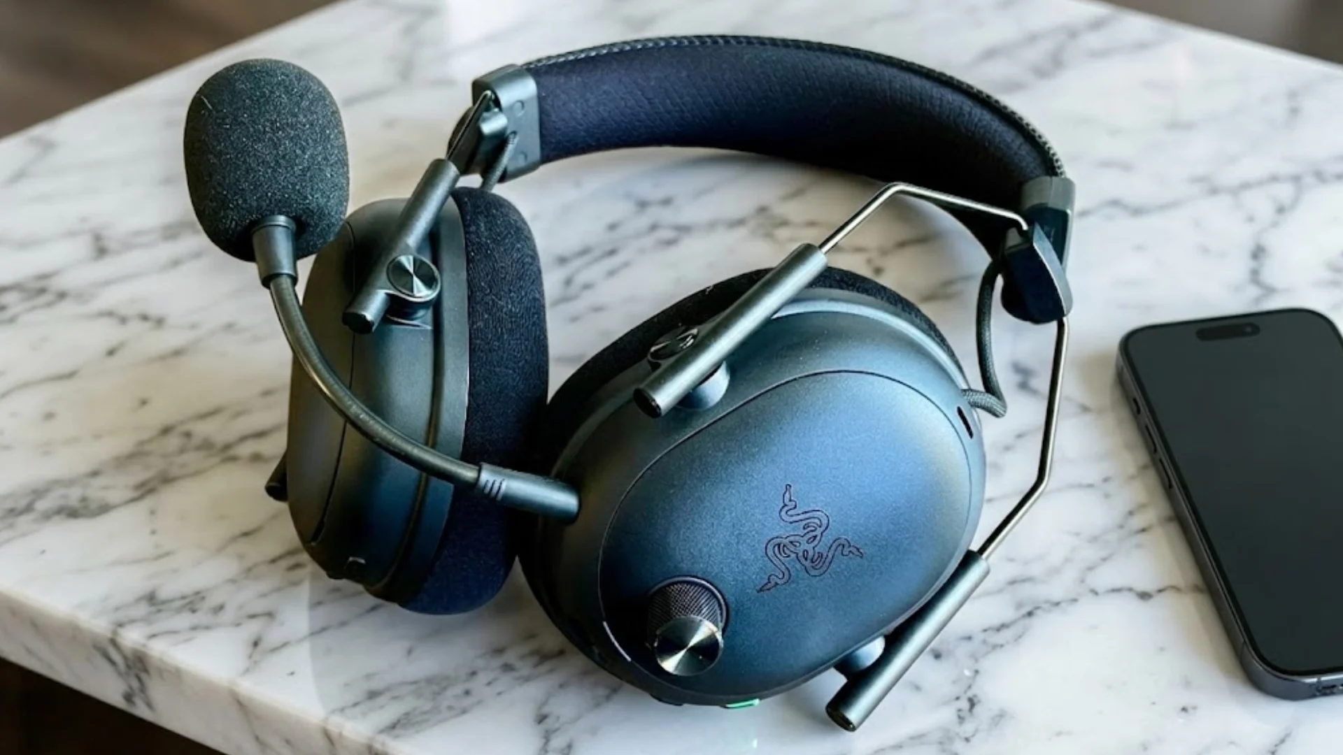 Razer BlackShark V3 gaming headset with boom mic and cushioned earcups placed on marble table beside smartphone
