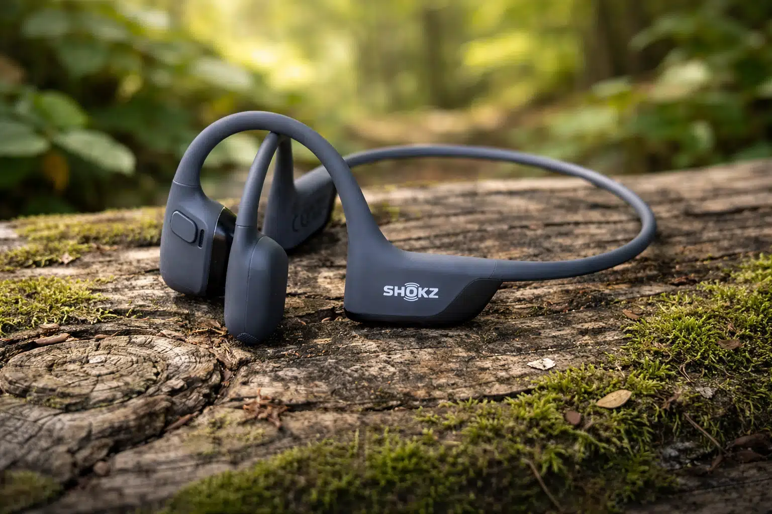 Shokz OpenRun Pro 2 bone conduction headphones resting on a mossy log outdoors
