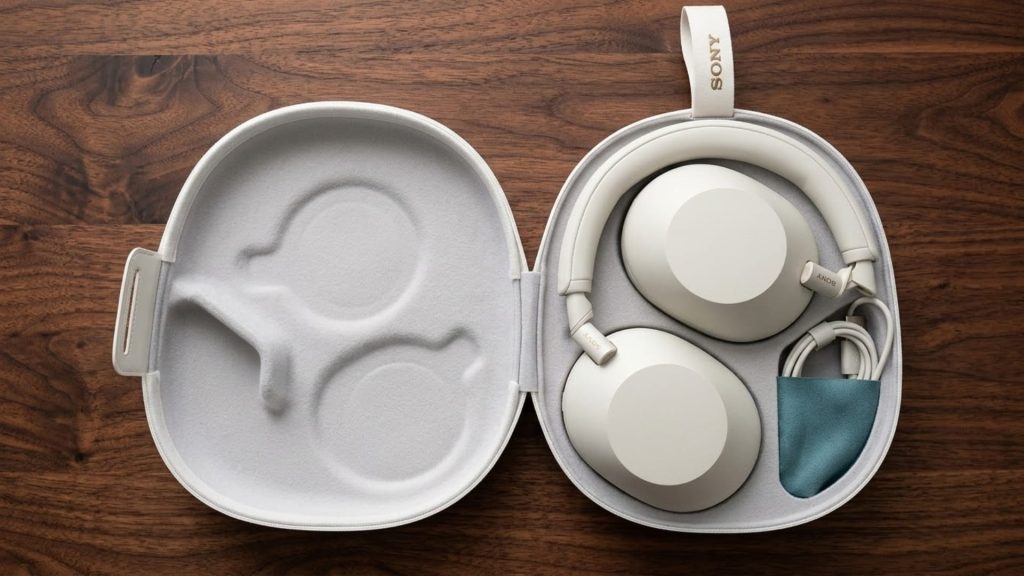 Sony WH-1000XM6 wireless headphones placed inside white carry case with charging cable and accessories on wooden surface