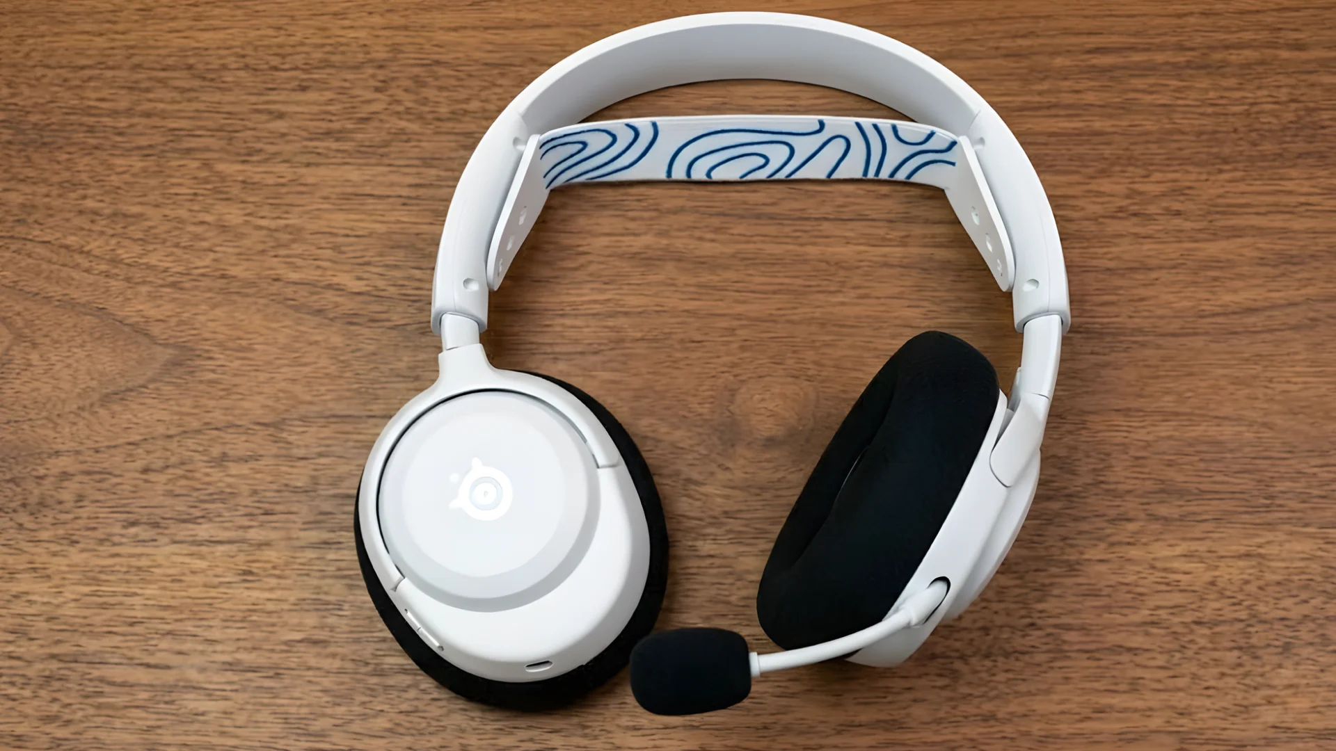SteelSeries Arctis Nova 5 Wireless with boom mic and black ear cushions placed on wooden surface, adjustable headband visible
