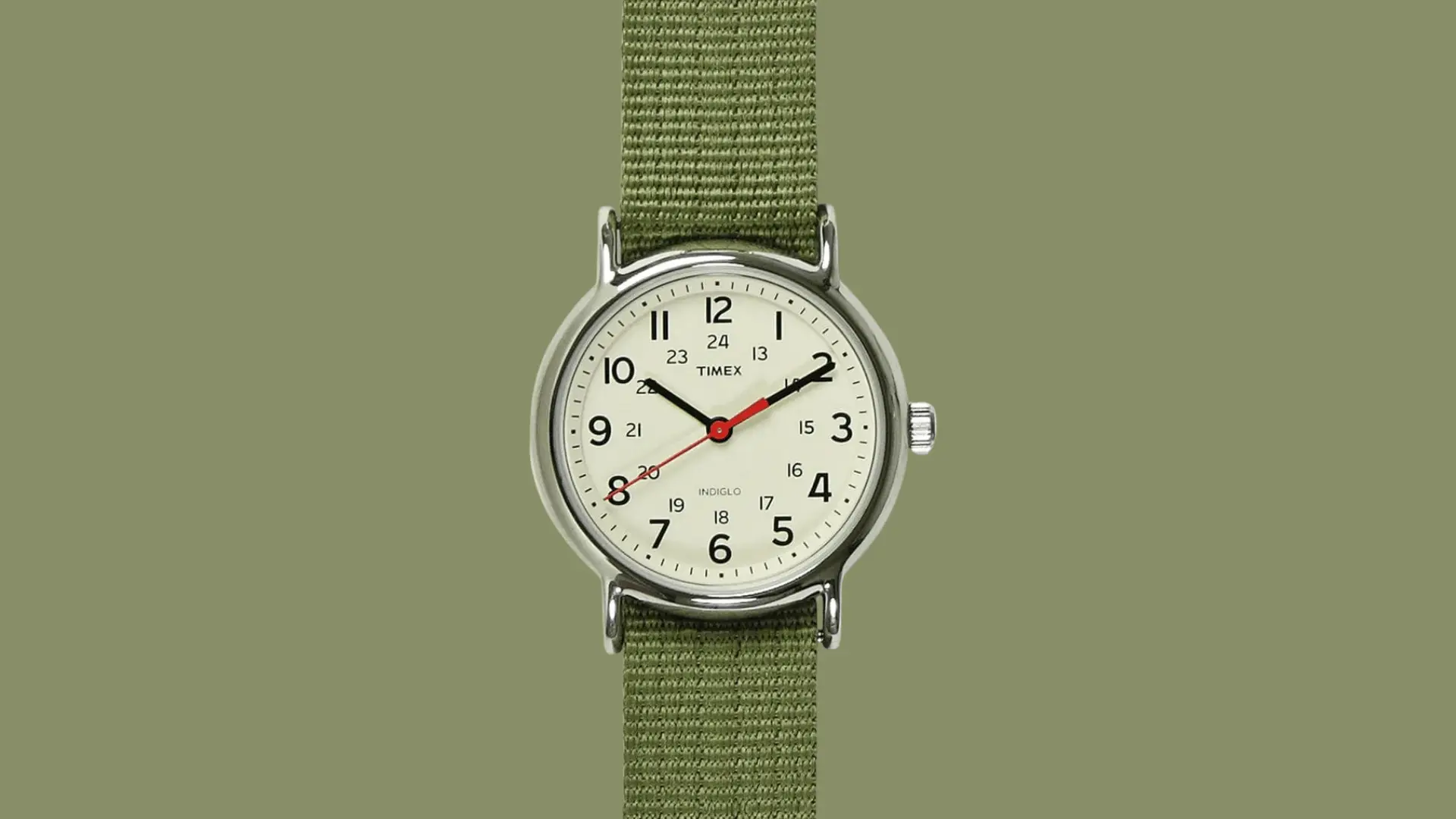 Timex field watch with cream dial, red second hand, and green fabric strap on a minimal olive background