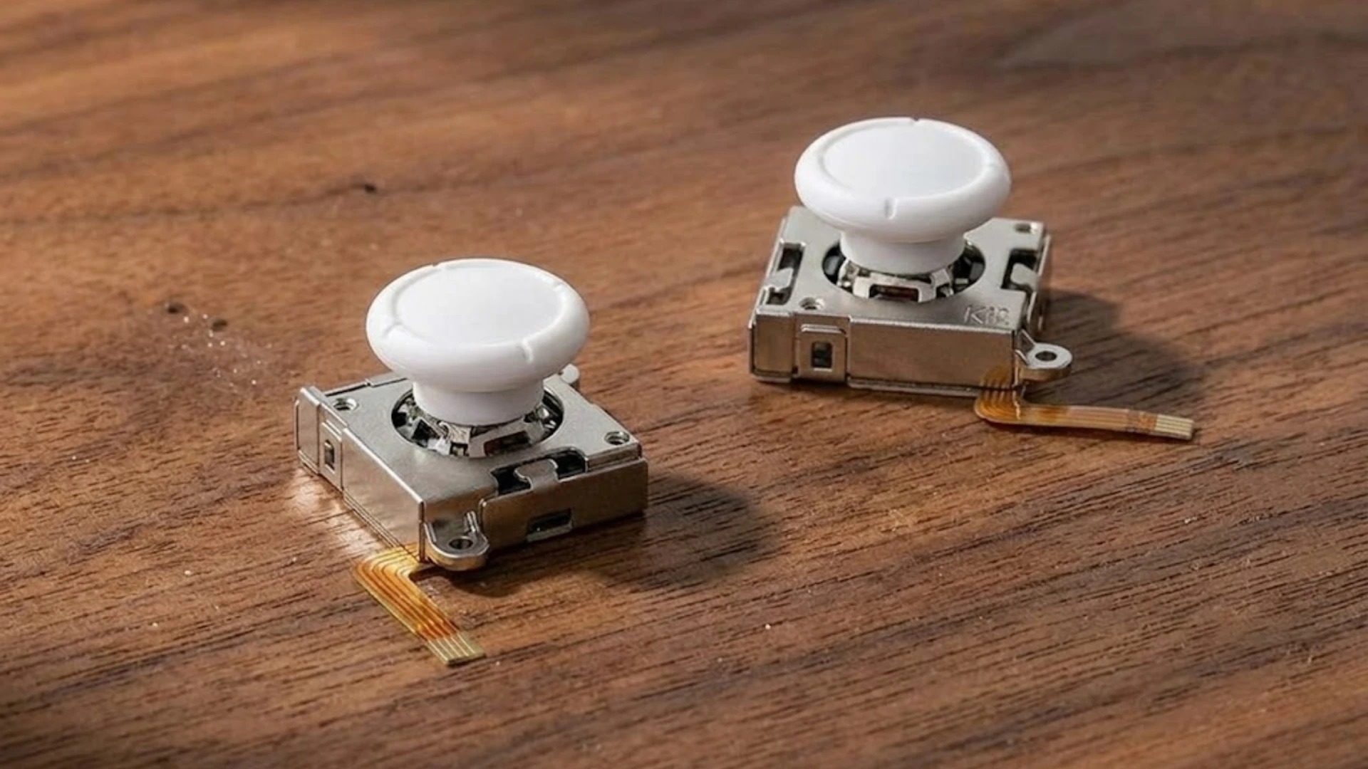 Two compact Hall Effect joystick modules with white caps placed on a wooden surface with ribbon cables visible