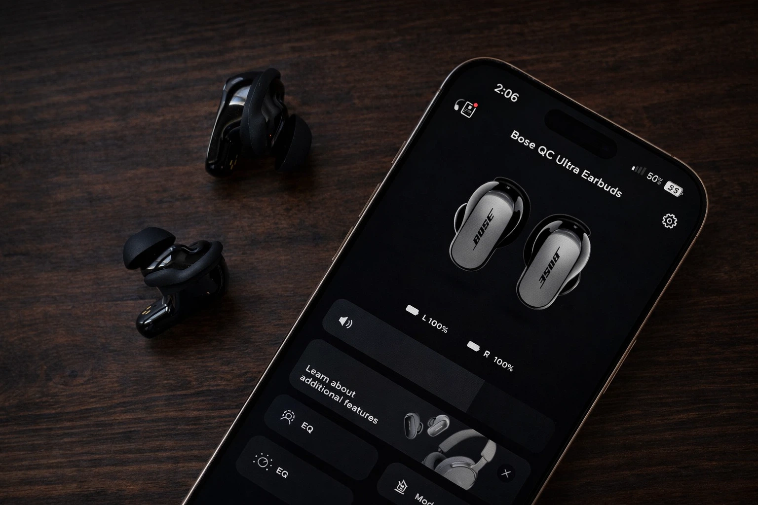 iPhone displaying Bose QuietComfort Ultra earbuds app interface with earbuds on table