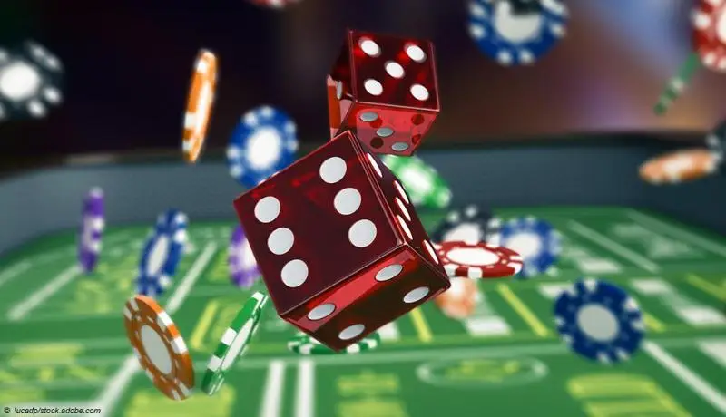 Red dice and colorful poker chips mid-air over a green casino table