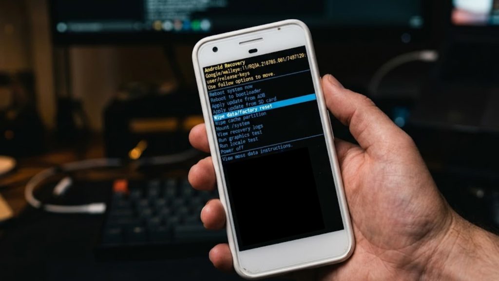 A close-up of a hand holding a white Android smartphone displaying Android Recovery Mode on screen