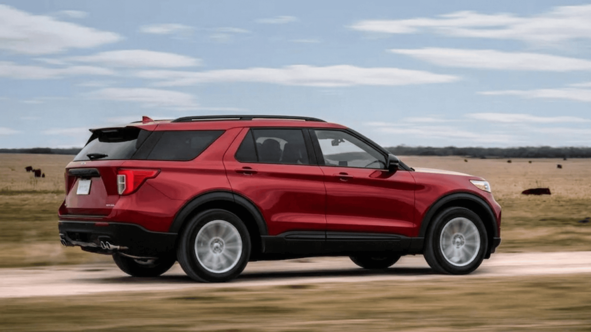 A side profile of a red Ford Explorer King Ranch SUV driving fast along a dirt road.