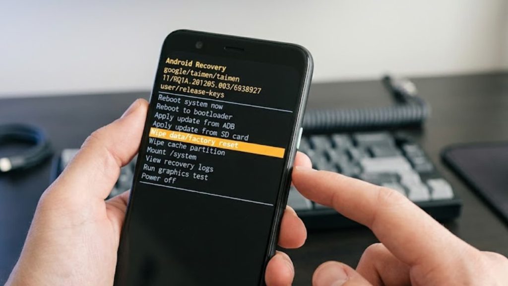 Android smartphone showing recovery mode menu on screen, user navigating options with volume buttons