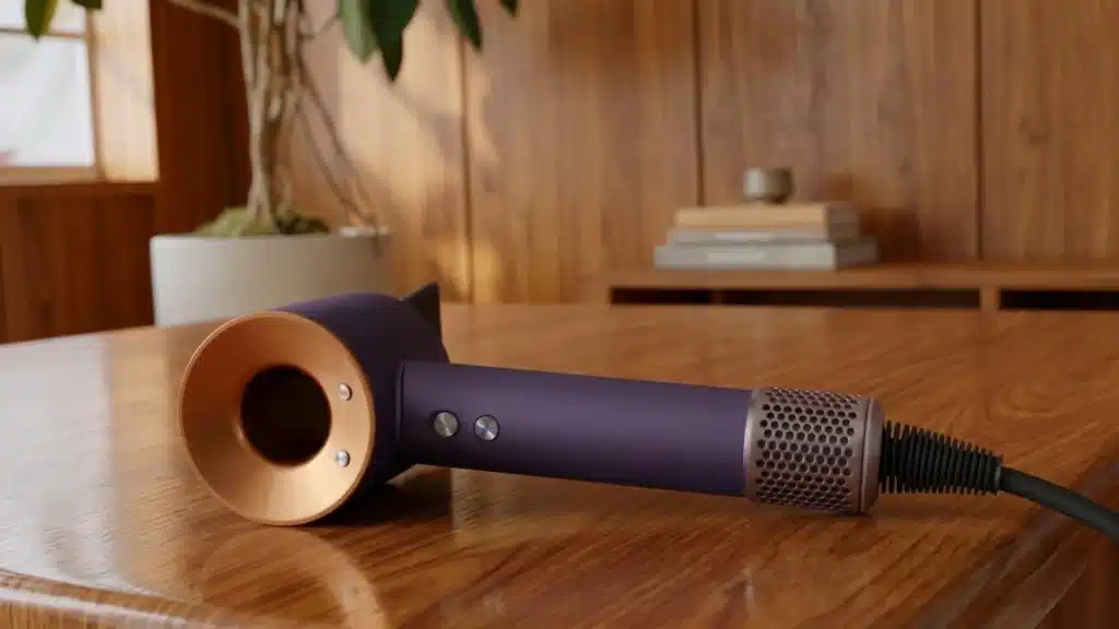 Dyson Supersonic hair dryer in purple and copper finish resting on a wooden table indoors