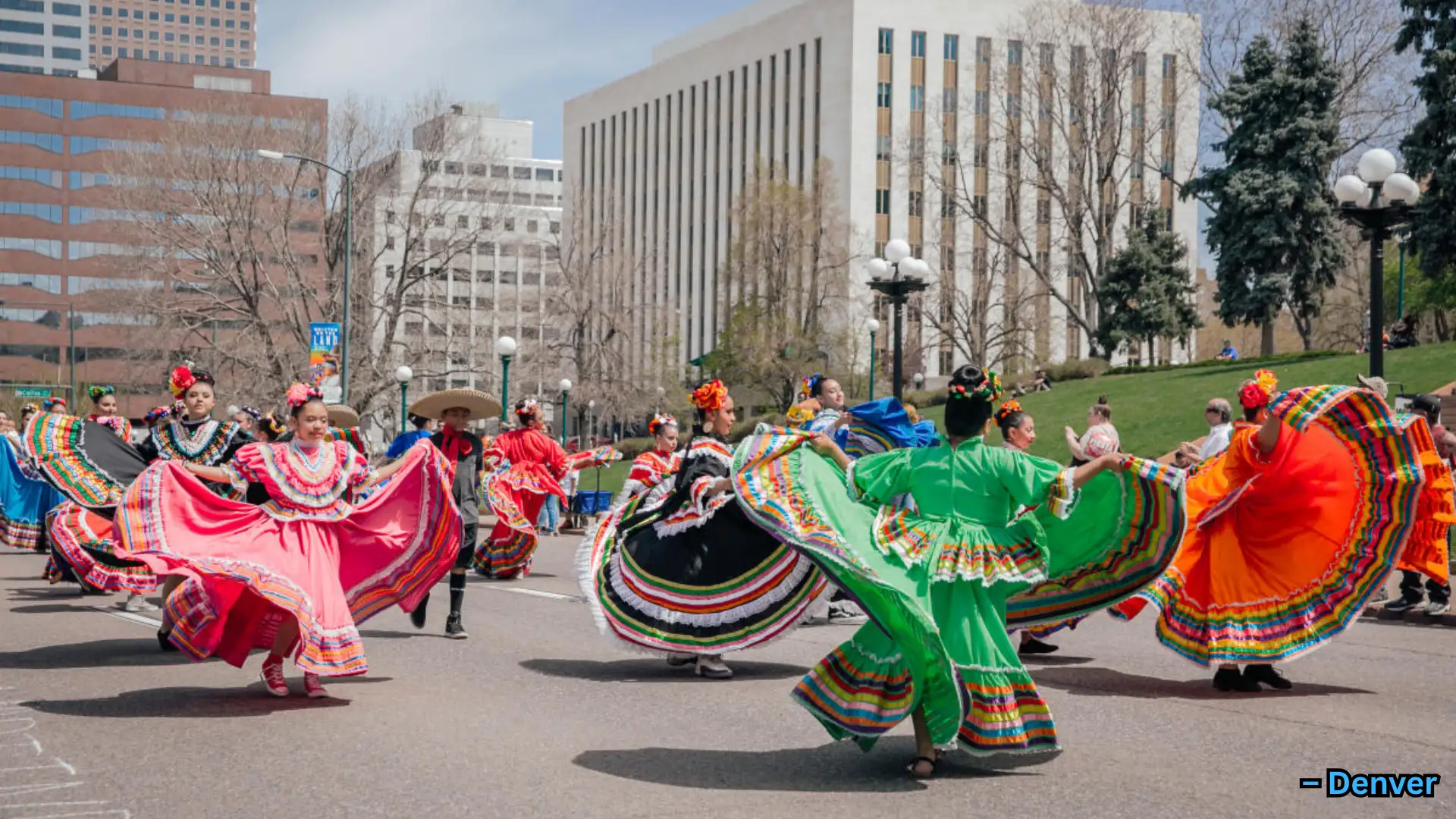 Group performing traditional dance in colorful dresses during street festival, city buildings visible in background