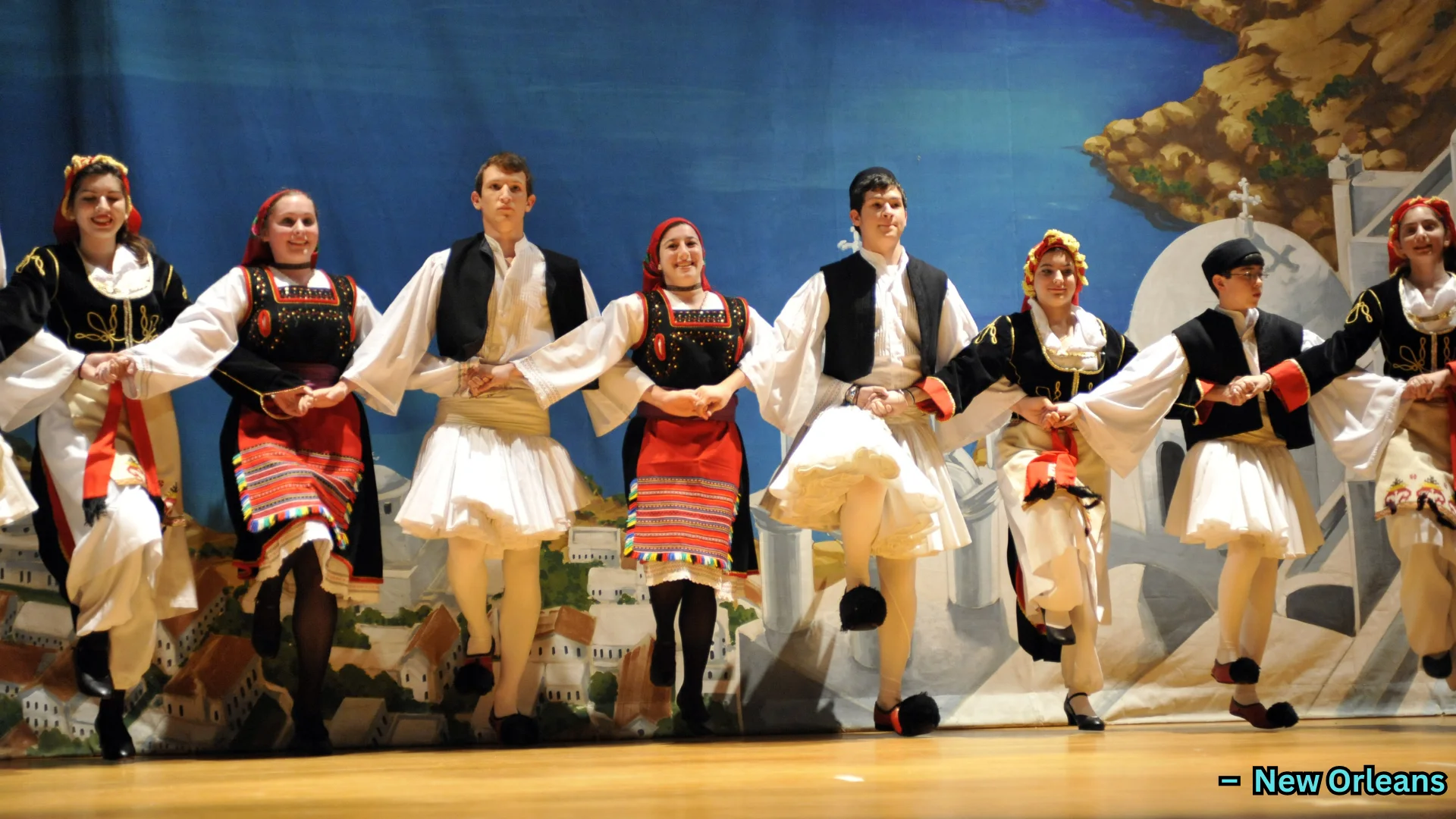 Group performing traditional folk dance on stage in cultural costumes, holding hands in coordinated formation