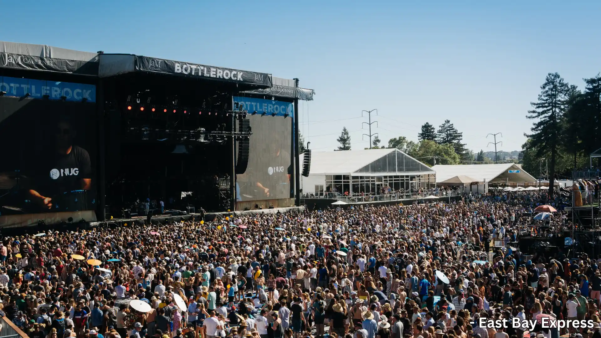 Large crowd at outdoor BottleRock music festival with stage, tents, and clear blue sky in background