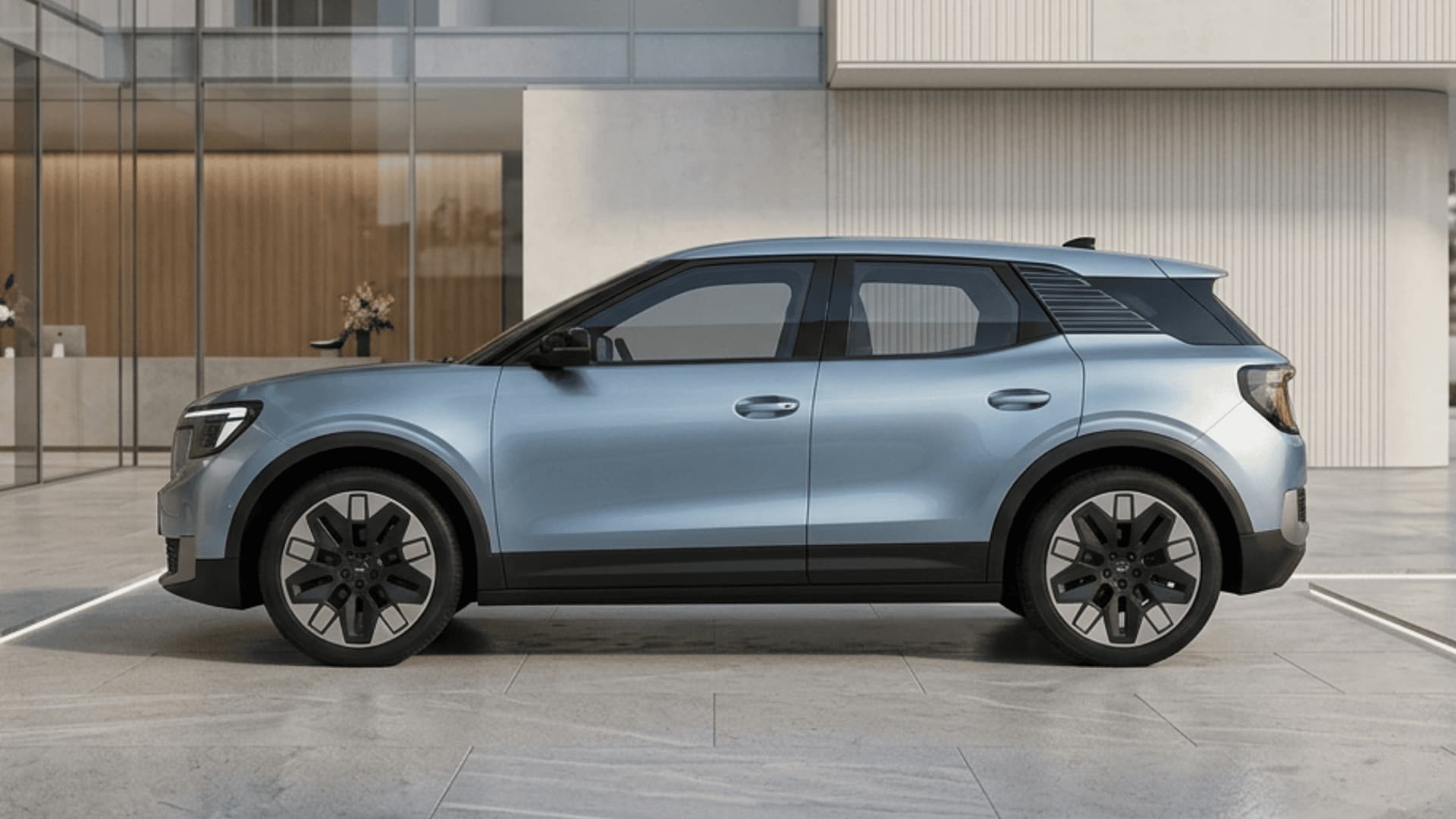 Light blue electric SUV parked on a paved plaza in front of a modern glass building