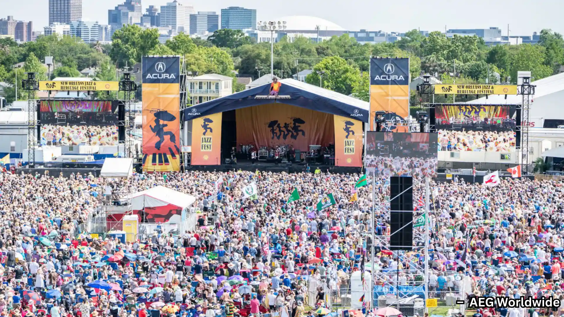 Massive crowd at New Orleans Jazz Fest, gathered before main stage with city skyline in background