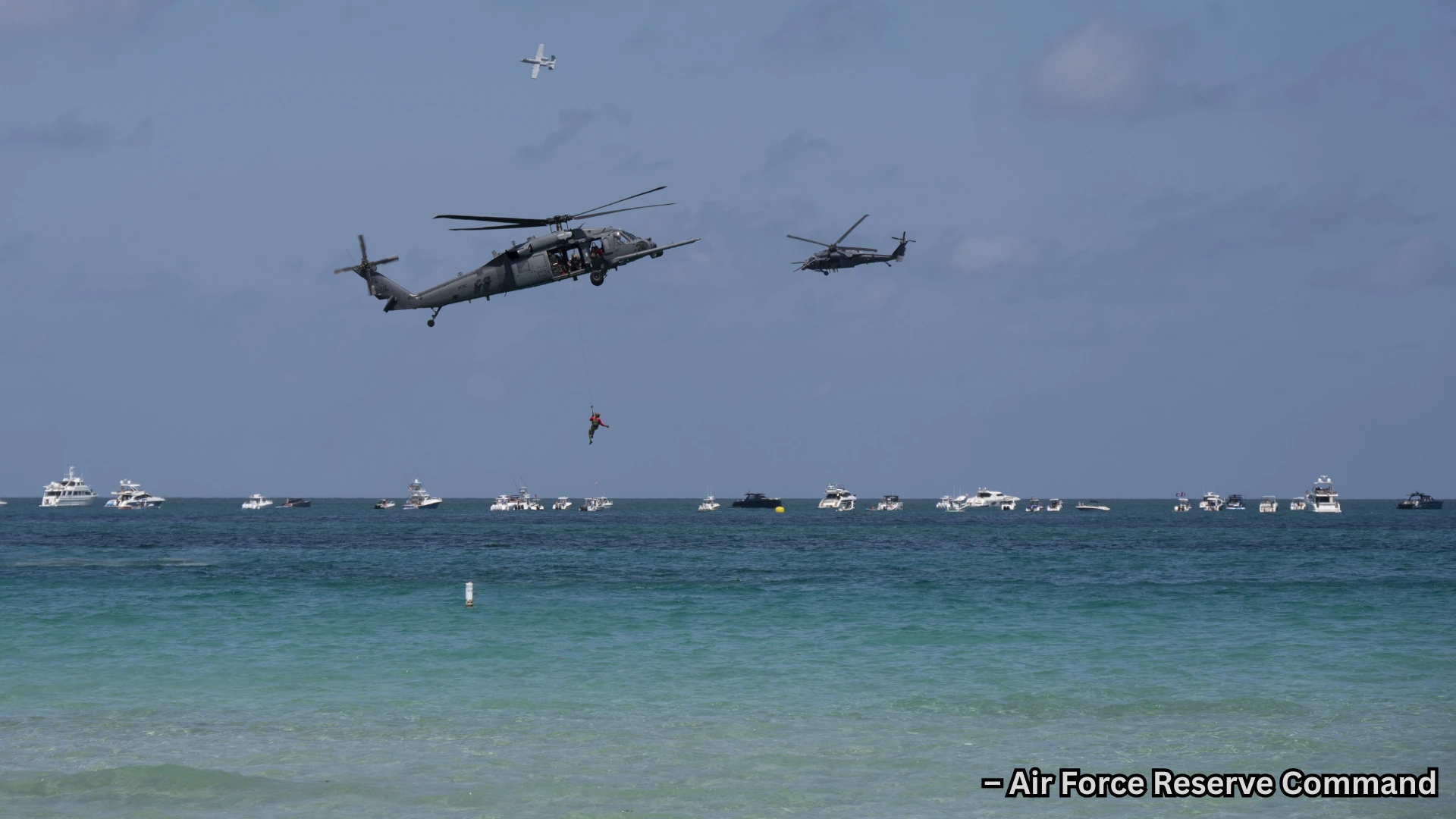 Military helicopters perform aerial display over ocean, lowering person while boats gather below in water