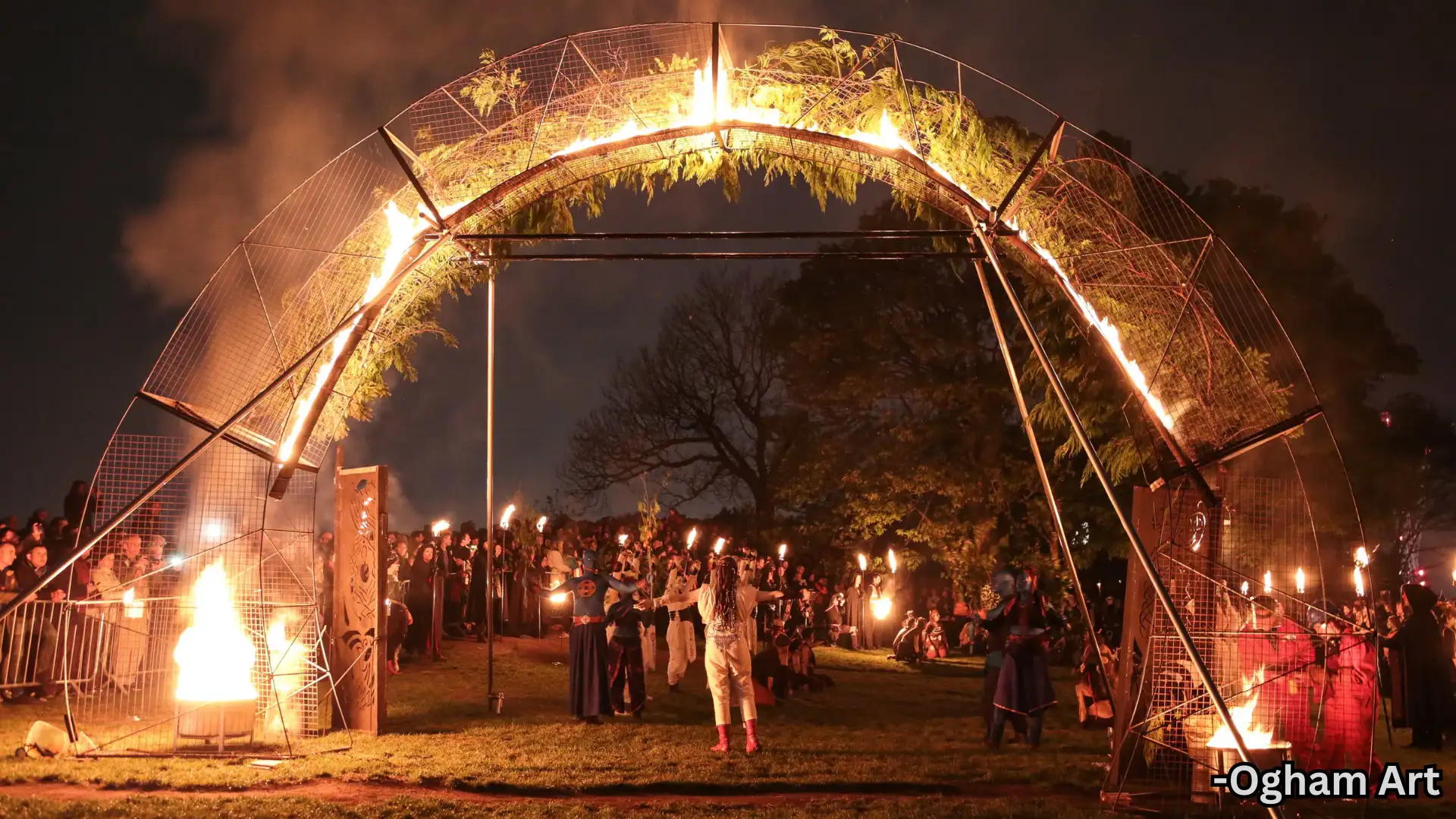 Night festival fire performance with flaming arch, performers and crowd gathered in outdoor park setting