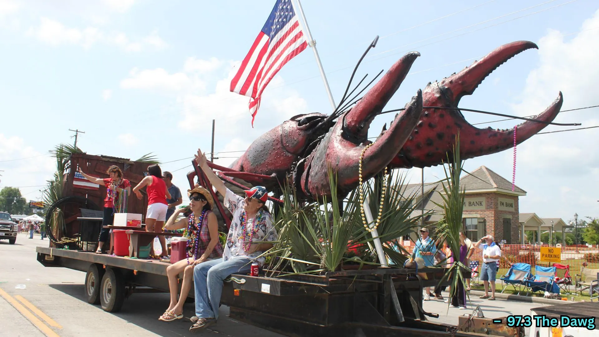 Parade float with giant crawfish sculpture, people riding and waving, American flag displayed during street celebration