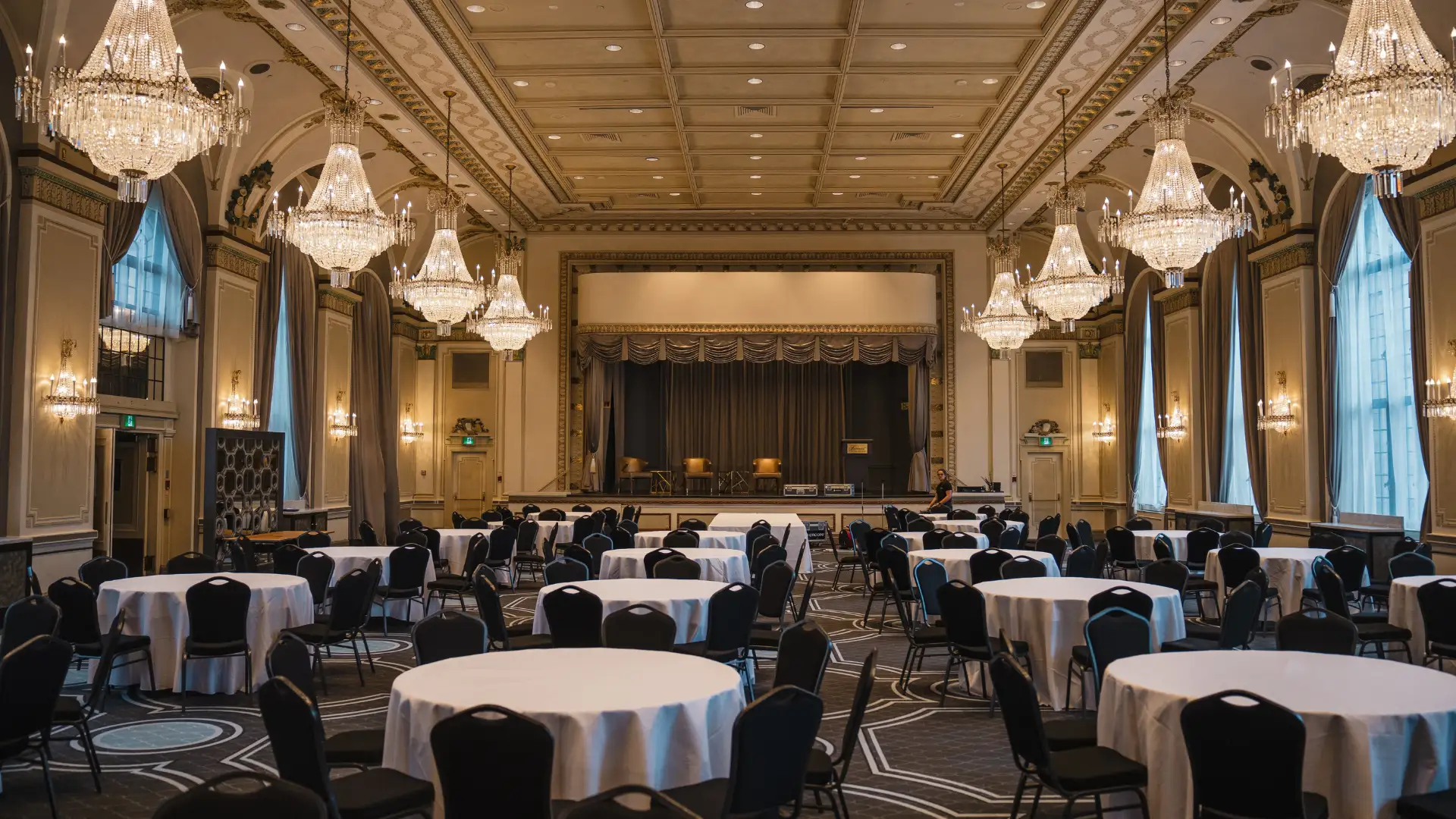 Spacious indoor banquet hall with large open layout, stage at the front, arranged round tables