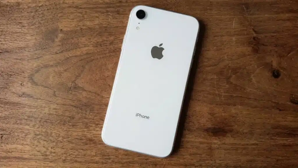 White iPhone XR placed on wooden surface showing back design with single camera and Apple logo clearly visible