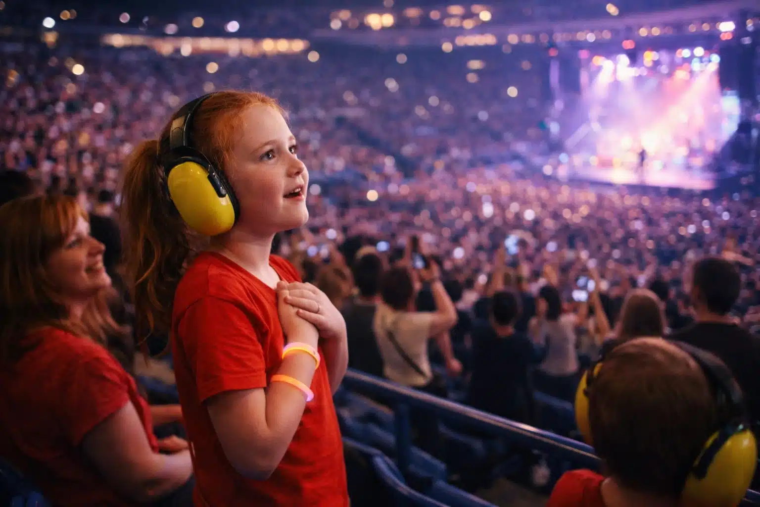 Young girl wearing ear protection watching live concert in crowded arena