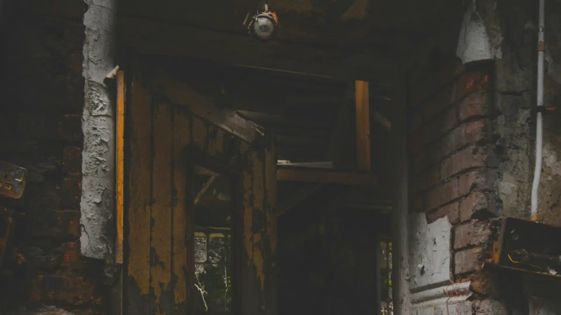 Abandoned, fire-damaged house interior with charred walls, broken structure, and dim lighting