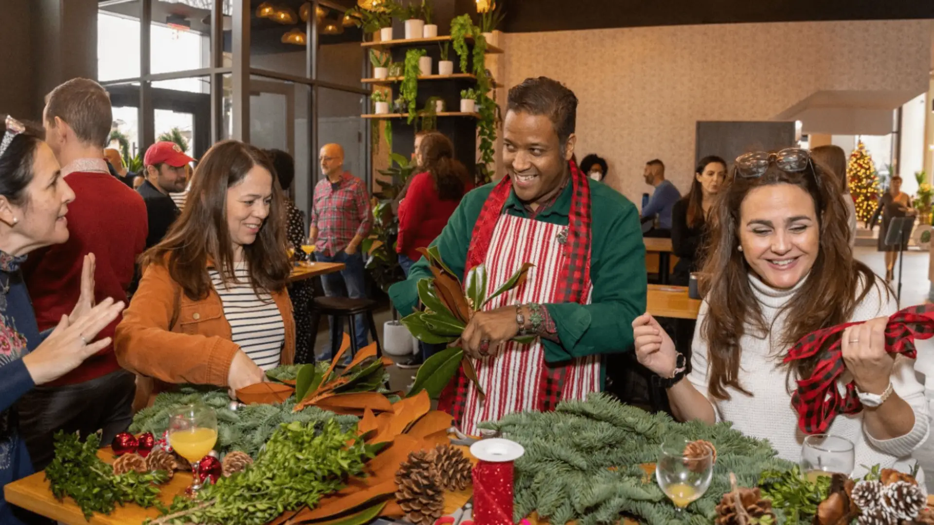 Adults crafting holiday wreaths with greenery, pinecones, and ribbons during a festive themed community event